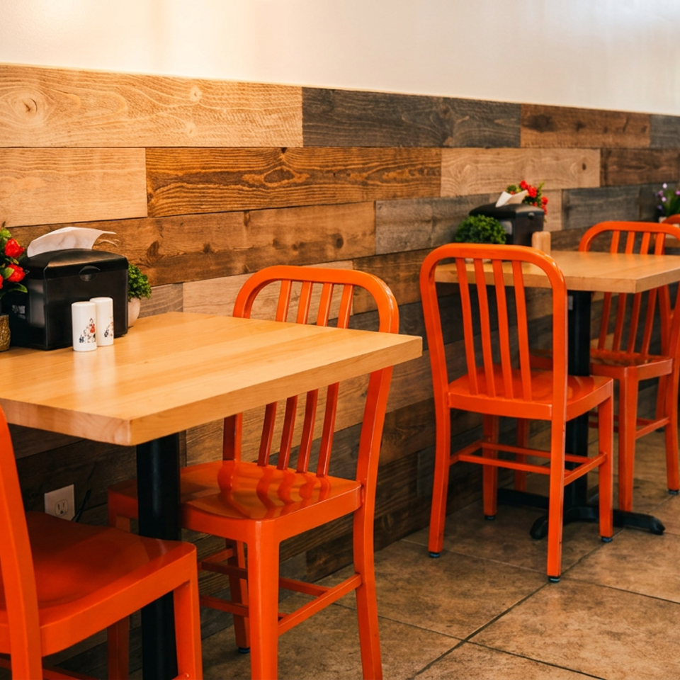 Restaurant dining area with wooden tables, bright orange chairs, floral centerpieces, and a rustic wood-paneled wall.