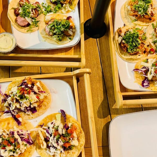 Overhead view of assorted tacos topped with cabbage, salsa, herbs, and sauces on wooden serving trays.