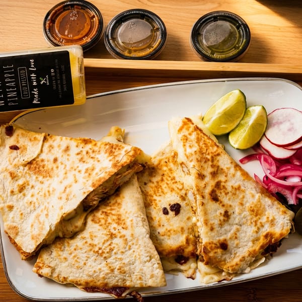 Grilled quesadilla wedges with lime, radishes, pickled onions, jalapeños, and dipping sauces on a wooden serving tray.
